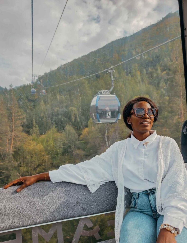 Woman riding inside a Shymbulak cable car with forested mountain scenery visible through the window.