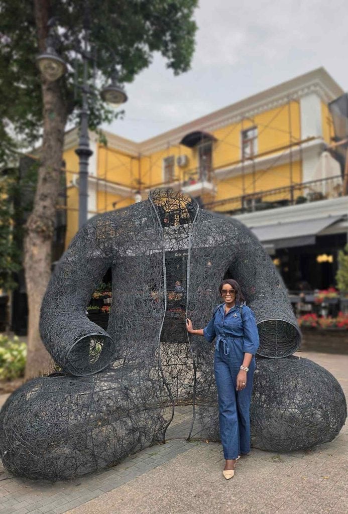 Woman traveler posing with a sculptural display along a tree-lined street in Kazakhstan.
