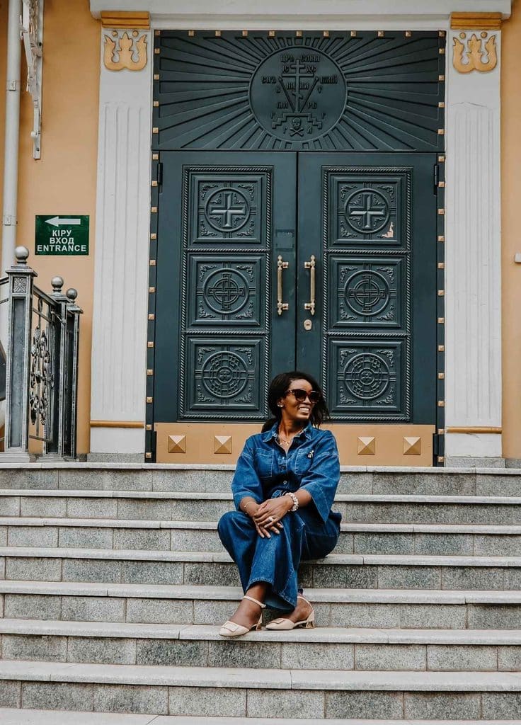 Black woman traveler sitting on the steps outside the ornate entrance of Ascension Cathedral in Almaty, Kazakhstan.