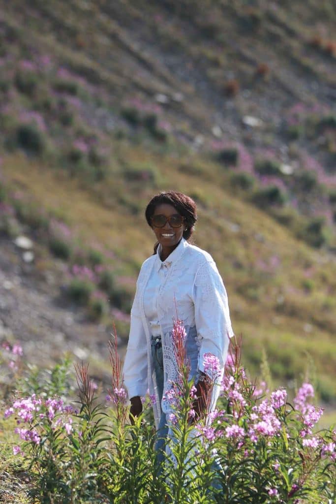 Black woman traveler standing among pink summer wildflowers in the scenic mountains of Kazakhstan