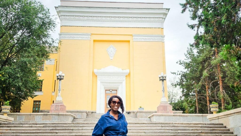 Woman standing outside a yellow historic building in Almaty during a Kazakhstan travel itinerary.