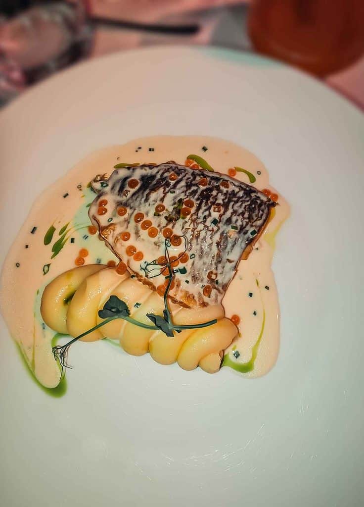 Restaurant dish in Kazakhstan featuring grilled fish served with creamy mashed potatoes, sauce, herbs, and small pearls of roe.