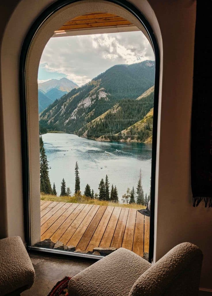 Scenic view of Kolsai Lake and the forested Tian Shan Mountains through a large arched window in Kazakhstan.