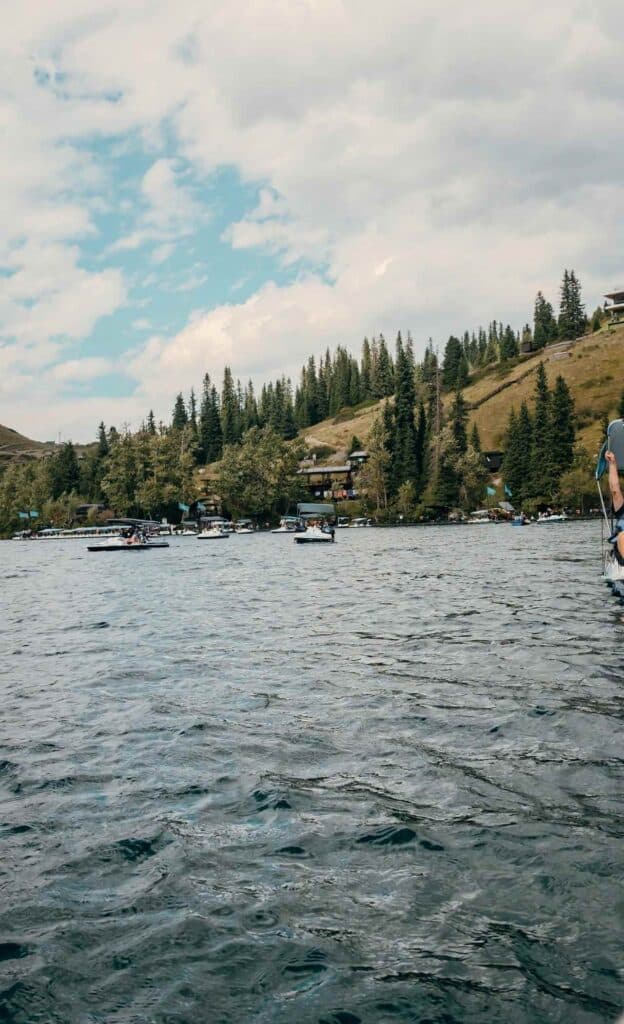 Visitors riding small boats across Lower Kolsai Lake beneath forested mountain slopes in Kazakhstan.