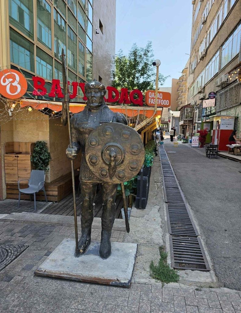 Bronze statue of a traditional Kazakh warrior holding a spear and shield on a city street in Almaty.