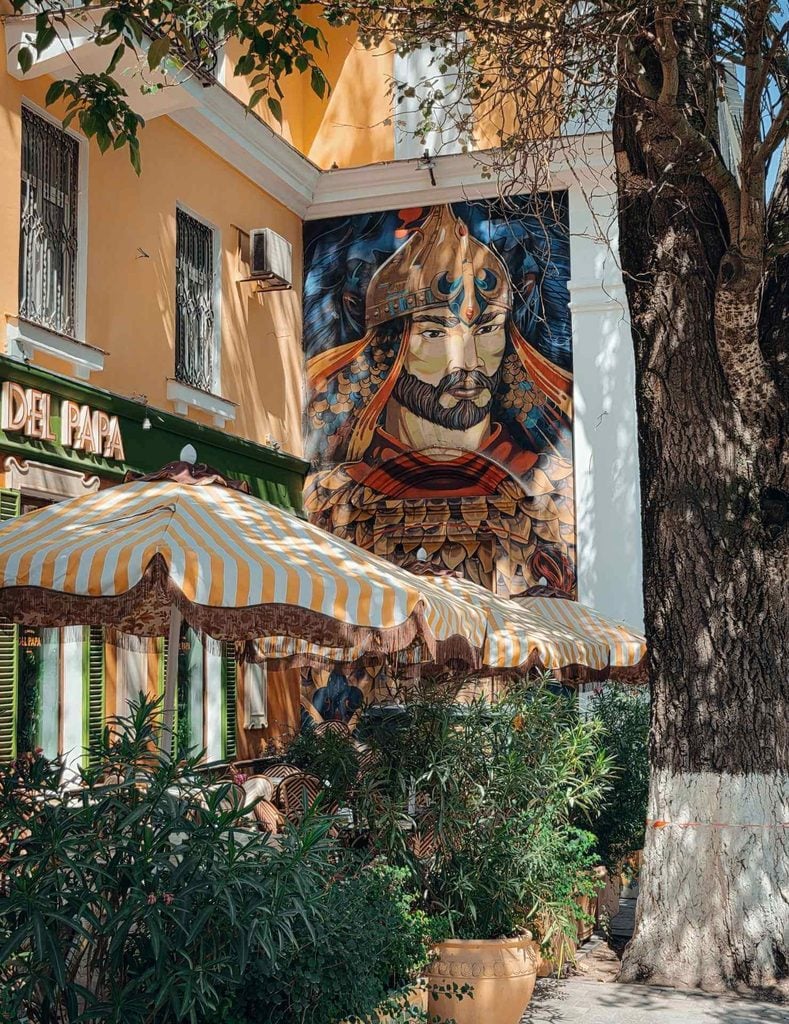 Colorful mural of a traditional Kazakh warrior painted on a building beside an outdoor café in Almaty.