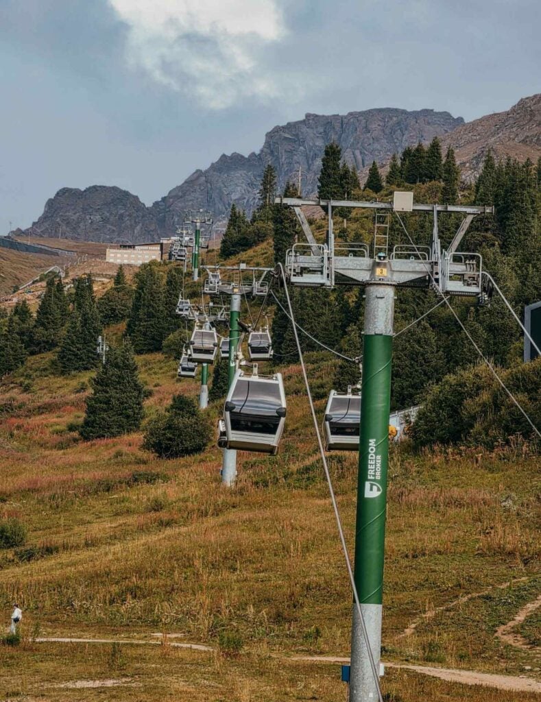 Shymbulak gondola cabins traveling above a forested slope in the Ile Alatau Mountains near Almaty.