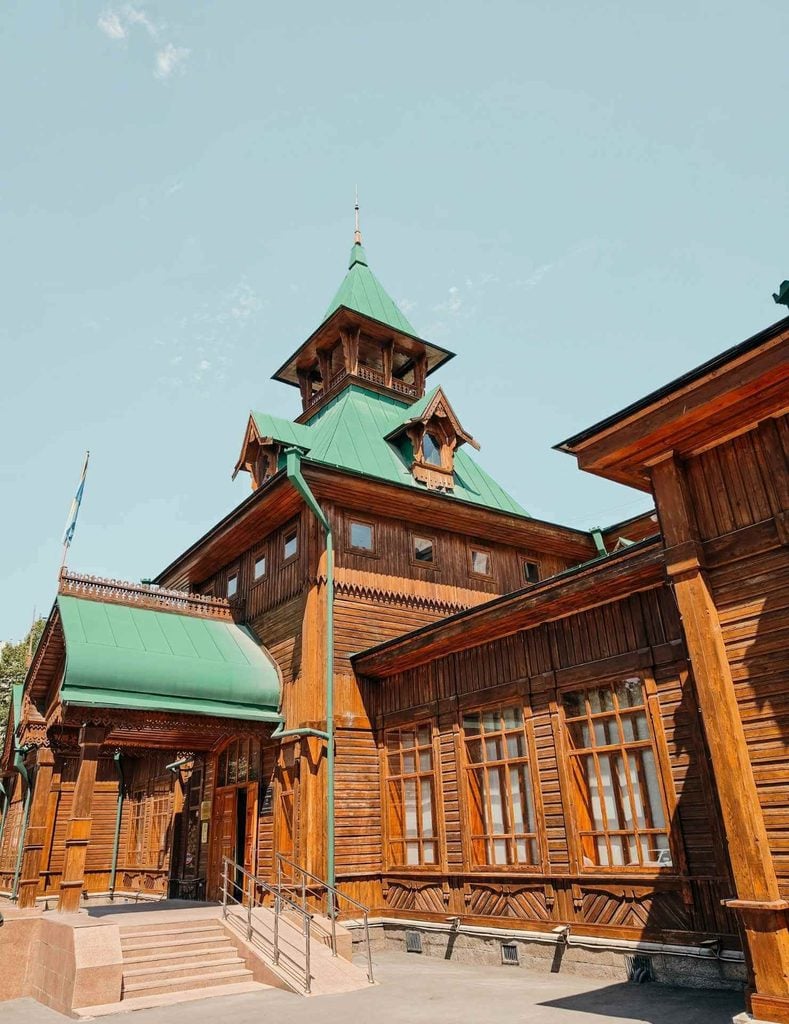 Historic wooden exterior and green roof of the Ykhlas Museum of Folk Musical Instruments in Panfilov Park, Almaty.